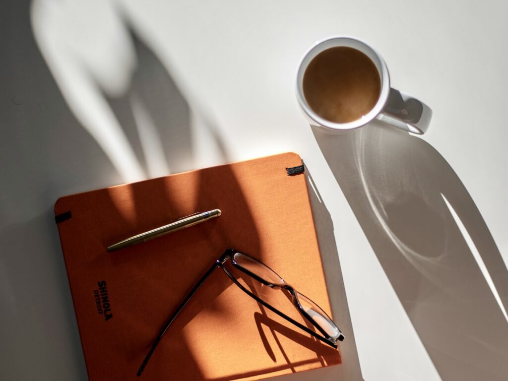 節約が楽しい朝のデスク。オレンジのノートとコーヒー